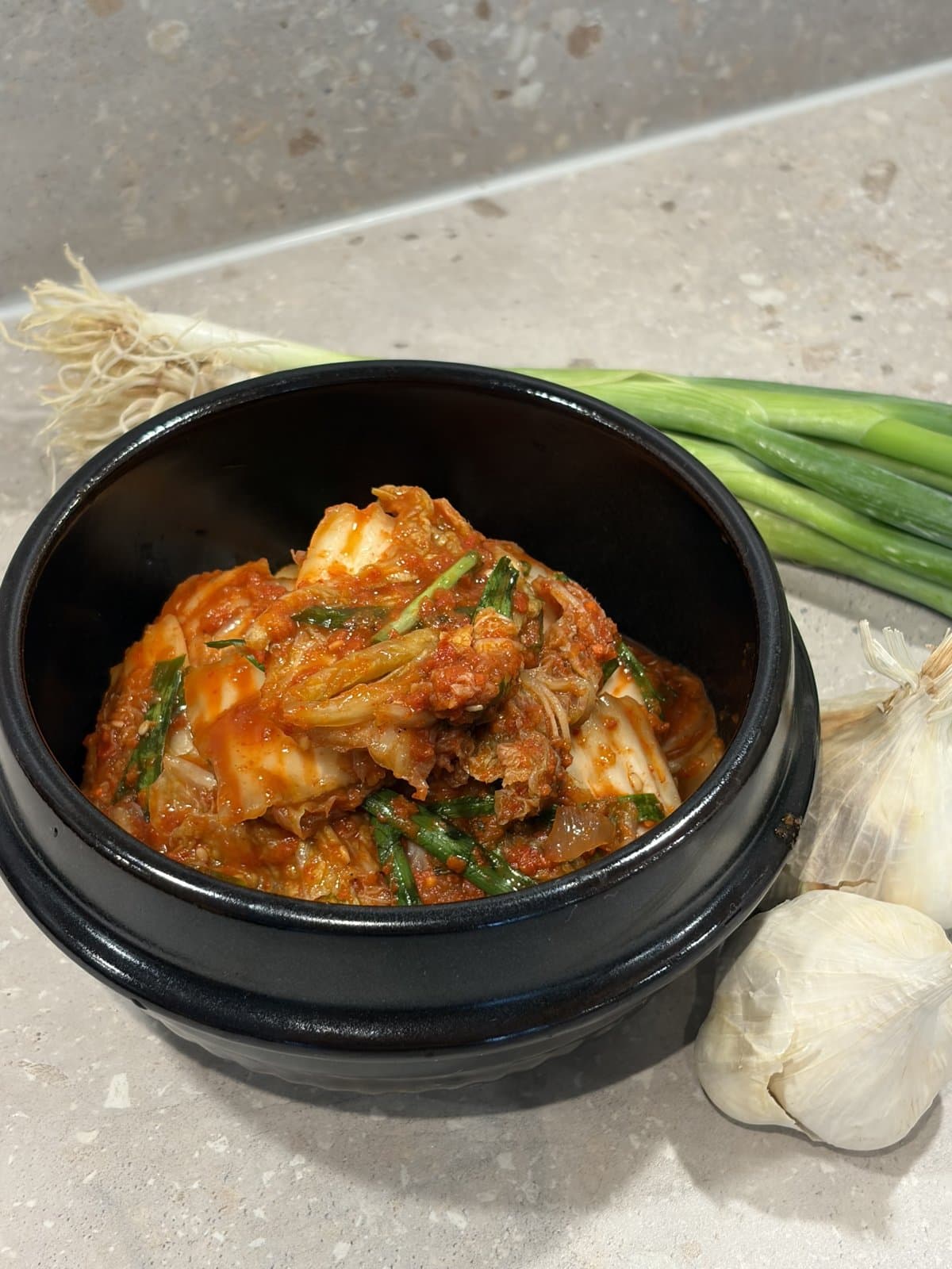 Mammas kimchi i en svart skål, med salladslök och vitlök bredvid